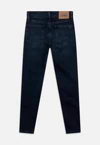 Ciemnoniebieskie obcisłe dżinsy z wysokim stanem, z beżową skórzaną naszywką, dwoma tylnymi kieszeniami i subtelnymi detalami szwów.