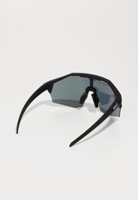 Schwarze achteckige Sonnenbrille mit matter Oberfläche, dunkeltönenden Gläsern und schlanken Bügeln, die auf der Innenseite eine strukturierte Griffoberfläche aufweisen.