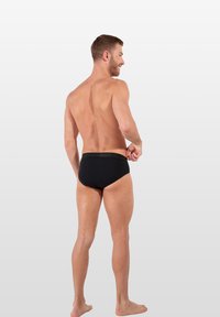 Schwarze Badehose mit glatter Textur, elastischem Bund und minimalistischem Design, von hinten an einem Model gezeigt.