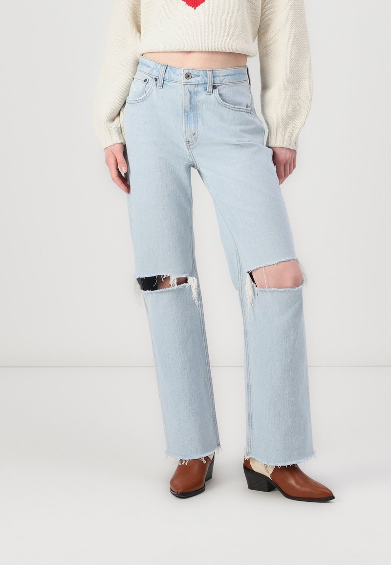 Ljusblå, högmidjade jeans med stora fransade knäskärningar och råa sidsömmar, ihop med bruna klackstövlar.