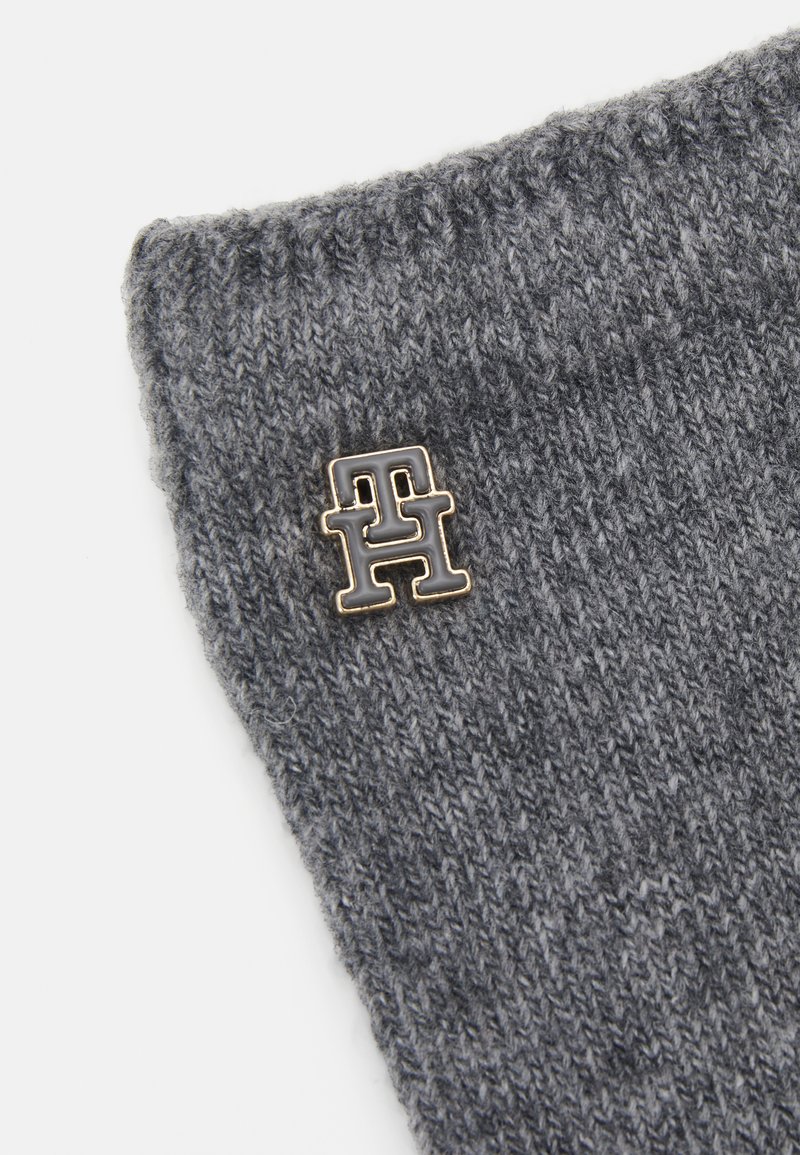 Szary dzianinowy beanie z podwiniętym brzegiem i małą, metalową pin-em logo w kolorze złotym i ciemnoszarym. Miękka tekstura i ciepły design.