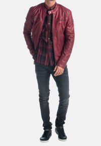 Rode leren jas met een hoge kraag en ritssluiting zakken, gedragen over een zwart geruit overhemd, gecombineerd met zwarte slim-fit jeans en sneakers.