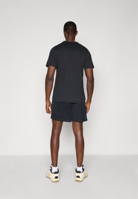 Sort kortærmet t-shirt og sorte shorts, parret med hvid- og sortfarvede athletic sko. Stofoverfladen ser glat ud, med minimal detaljering.