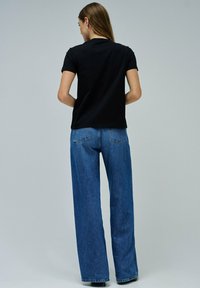 Camiseta negra de manga corta combinada con jeans anchos de talle alto en color azul. La tela parece suave, con una textura lisa y un detalle mínimo.