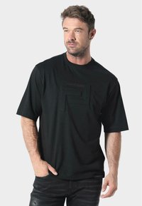 Camiseta negra de manga corta con un logo negro en relieve en el pecho, hecha de una tela suave. Presenta un ajuste relajado y un escote redondo.