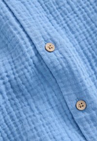 Tissu bleu clair texturé avec un motif en nid d'abeille et deux boutons ronds beiges cousus sur un rabat.