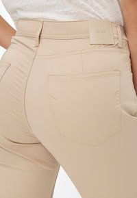 Beige slim-fit broek met een gladde textuur, voorzien van een achterzak, een slank ontwerp en een label op de tailleband.