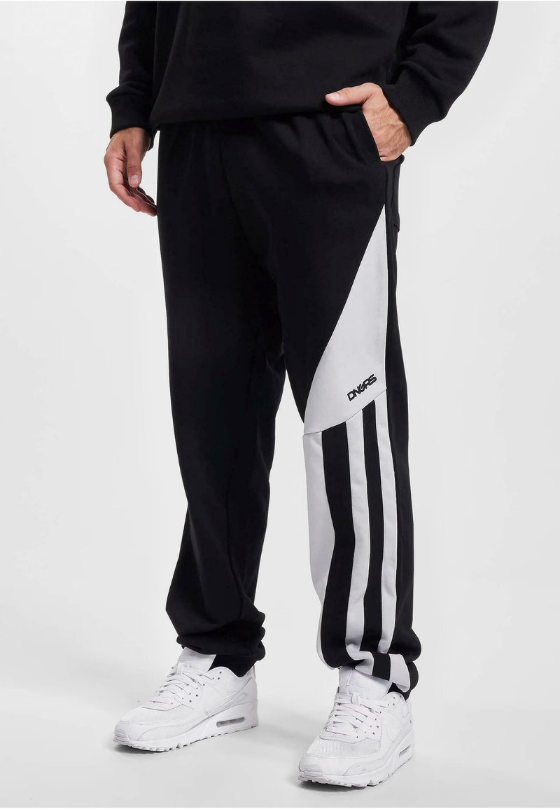 Schwarze Sweatpants mit weißen Seitenstreifen, featuring diagonales Design und drei vertikale Streifen. Hergestellt aus weichem Stoff mit seitlichen Taschen.