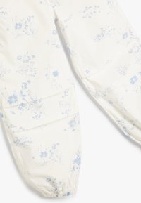 Blomsterprintbukser med hvid baggrund og lyseblå blomster. Elastiske manchetter ved anklerne, lavet af letvægtstof.