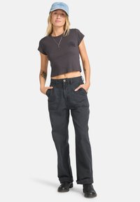 Camiseta corta negra de manga corta, con un gráfico en el pecho. Pantalones negros de tiro alto y corte holgado, con bolsillos laterales y cierre de botón.