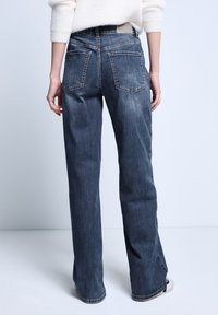 Jeans de mezclilla de lavado oscuro con un ajuste de pierna recta, que cuentan con dos bolsillos traseros y un ligero desvanecimiento en la tela; sin logos ni patrones visibles.