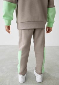 Hellbraunes Sweatshirt- und Jogginghosen-Set mit mintgrünen Akzenten. Glatter Stoff, lockere Passform und elastische Bündchen. Weiße Sneaker sichtbar.