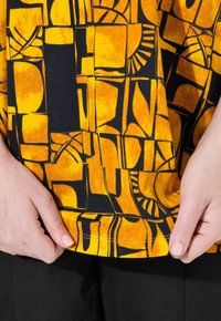 Camicia in tessuto giallo e nero con motivi geometrici e forme astratte, realizzata in un tessuto liscio e leggero.