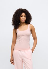 Šviesiai rožinė tank top tipo palaidinė iš minkštos, tamprios medžiagos su kvadratiniu iškirpimu ir siaurais petnešėliais. Apačioje subtiliai siuvinėta apačia ir logotipo detalė.
