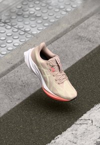 Lichtbeige sport schoen met een gestructureerde upper, roze accenten en een witte zool. Heeft een ronde neus en subtiele logo-details.