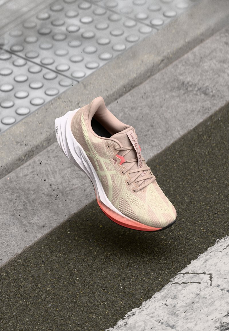 Lichtbeige sport schoen met een gestructureerde upper, roze accenten en een witte zool. Heeft een ronde neus en subtiele logo-details.