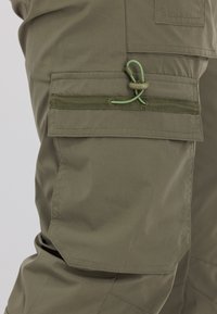 Nahaufnahme von olivgrüner Cargo-Hosen-Tasche mit Klappe und verstellbarem Kordelzug am Oberschenkel.