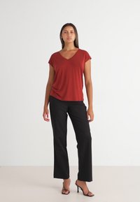 Rode v-hals t-shirt met korte mouwen, gecombineerd met zwarte wijde broek en zwarte hoge hakken. Effen achtergrond.