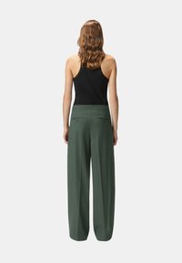 Pantalones anchos de pierna verde con una textura suave, que presentan una cintura alta, dos bolsillos traseros y un corte recto. Lleva una camiseta sin mangas negra.
