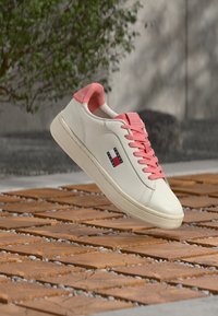 Λευκό δερμάτινο αθλητικό παπούτσι με ροζ τακούνι και κορδόνια, με υφή στη μύτη και ένα μικρό λογότυπο στη πλευρά.