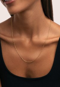 Collier en chaîne dorée avec des maillons allongés, présentant une finition lisse. Porté sur un haut noir côtelé, accentuant le décolleté.