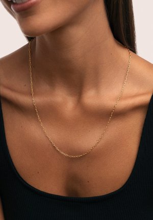 Collier en chaîne dorée avec des maillons allongés, présentant une finition lisse. Porté sur un haut noir côtelé, accentuant le décolleté.