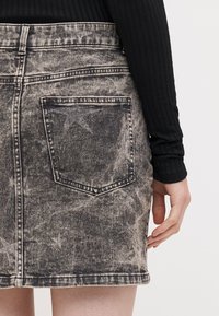 Svart denim mini skjørt med falmet stjerne mønster, baklomme detaljer, frynset kant, og en lett slitt finish. Kombinert med en svart langermet topp.