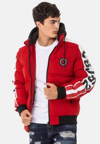 Red puffer jacket with a black hood, featuring white striped accents on the sleeves and a circular logo on the chest. Zippered front.