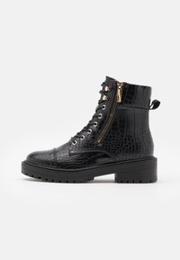 Botín negro de charol con diseño de cocodrilo, con suela gruesa, cremallera dorada lateral y tira en la parte trasera.