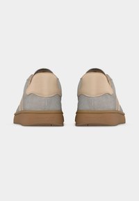 Ζευγάρι γκρι και μπεζ αθλητικά παπούτσια χαμηλού ύψους με καφέ σόλες από καουτσούκ, φαίνονται από πίσω σε λευκό φόντο.