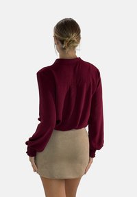 Bordeaux blouse met een ontspannen pasvorm, lange mouwen en een textuurstof, gecombineerd met een beige suède minirok.