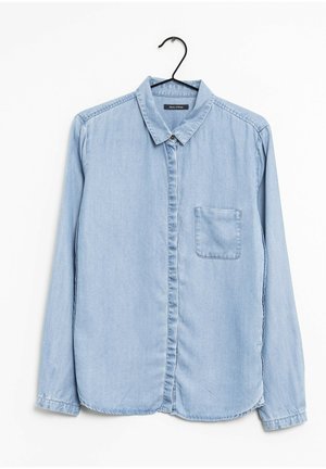 Jasnoniebieska denimowa koszula z długim rękawem, kołnierzykiem, przednią kieszenią na piersi, zapięciem na guziki, zawieszona na czarnym wieszaku na białym tle.