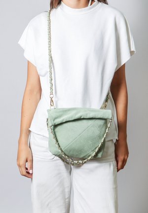 Sac bandoulière en suede vert avec un motif matelassé, quincaillerie dorée et une bandoulière en chaîne composée de maillons alternés verts et dorés.