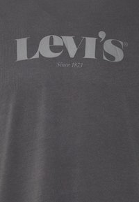 Camiseta de algodón gris oscuro con un gran logo blanco de "Levi's" y el texto "Desde 1873" debajo. Textura suave, diseño de cuello redondo.