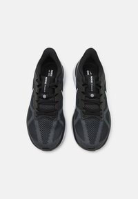 Black athletic shoes with a mesh upper, textured pattern, laces, and a white logo; featuring a cushioned sole and rounded toe design.