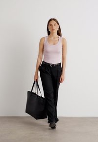 Musta olkalaukku, istuva vaaleanpunainen ribbaa tanktoppi, mustat housut ja tummat kengät. Malli seisoo neutraalilla taustalla. Yksinkertainen ja minimalistinen muotoilu.