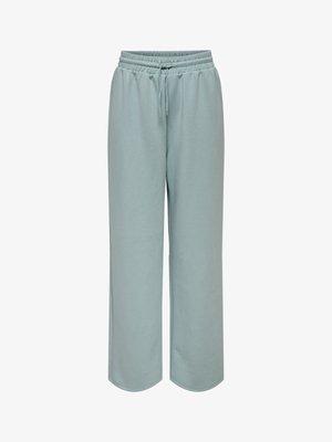 Pantalon de survêtement large bleu clair en tissu doux. Équipé d'une taille élastique avec cordon de serrage et de poches latérales. Texture lisse.