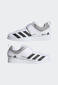 Zapatillas deportivas blancas con parte superior de malla, franjas negras y una correa de velcro. Suela blanca gruesa con detalles texturizados y marca en el costado.