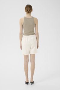 Lys beige tank topp med ribbet tekstur, kombinert med kremfargede, knelange shorts med elastisk midje. Svarte hælhæler.