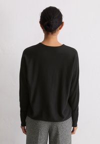 Schwarzer Strickpullover mit entspannter Passform, abgesenkten Schultern und rundem Ausschnitt, kombiniert mit grauen strukturierten Hosen.