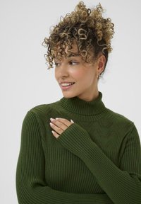 Tumši zaļš ribotais adījums ar augstu apkakli, kas izceļas ar teksturētu rakstu un pagarinātām piedurknēm, piedāvājot vieglu un mājīgu dizainu.