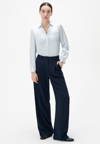 Chemise en satin bleu clair à manches longues avec deux poches poitrine, associée à un pantalon large bleu marine foncé avec une fermeture à double bouton.