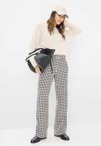 Crème trui, broek met een pied-de-poule patroon in zwart en wit, zwarte leren handtas en beige pet. Schoeisel: zwarte, platte schoenen.