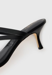 Black high-heeled sandal with two thin straps, smooth texture, open toe design, and curved heel. Gold branding on the insole.