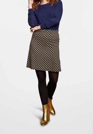 Een bruine rok met patroon toont geometrische vormen in groen en blauw. Het is gecombineerd met zwarte panty's en glanzende gouden enkellaarsjes.