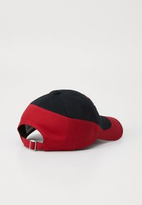 Red and black baseball cap featuring a curved brim, adjustable back strap, and contrasting color blocks with visible stitching detail.