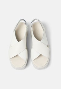 Sandali bianchi con cinturini incrociati in pelle liscia. Suola spessa e interno testurizzato. Dettagli metallici sul tallone.