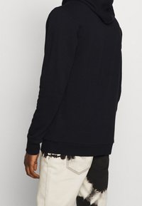 Marinblå hoodie med texturerat tyg, kenguruficka och justerbar huva. Bärs med vita och svarta tie-dye byxor.