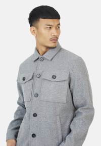 Grijze wolmix jas met een kraag, zes voorknoopsluitingen en twee borstzakken met kleppen. Soepele textuur met een getailleerde pasvorm.