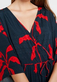 Vínová wrap šaty z látky s červeným listovým vzorem, hlubokým V-čkovým výstřihem a krátkými rukávy s detailem vázání v pase.